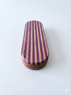 Oval-shaped wooden object with purple  heart and cherry wood stripes on top and a solid cherry wood bottom