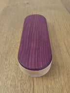 Oval-shaped wooden object with a purple top and white bottom on a light oak-colored surface