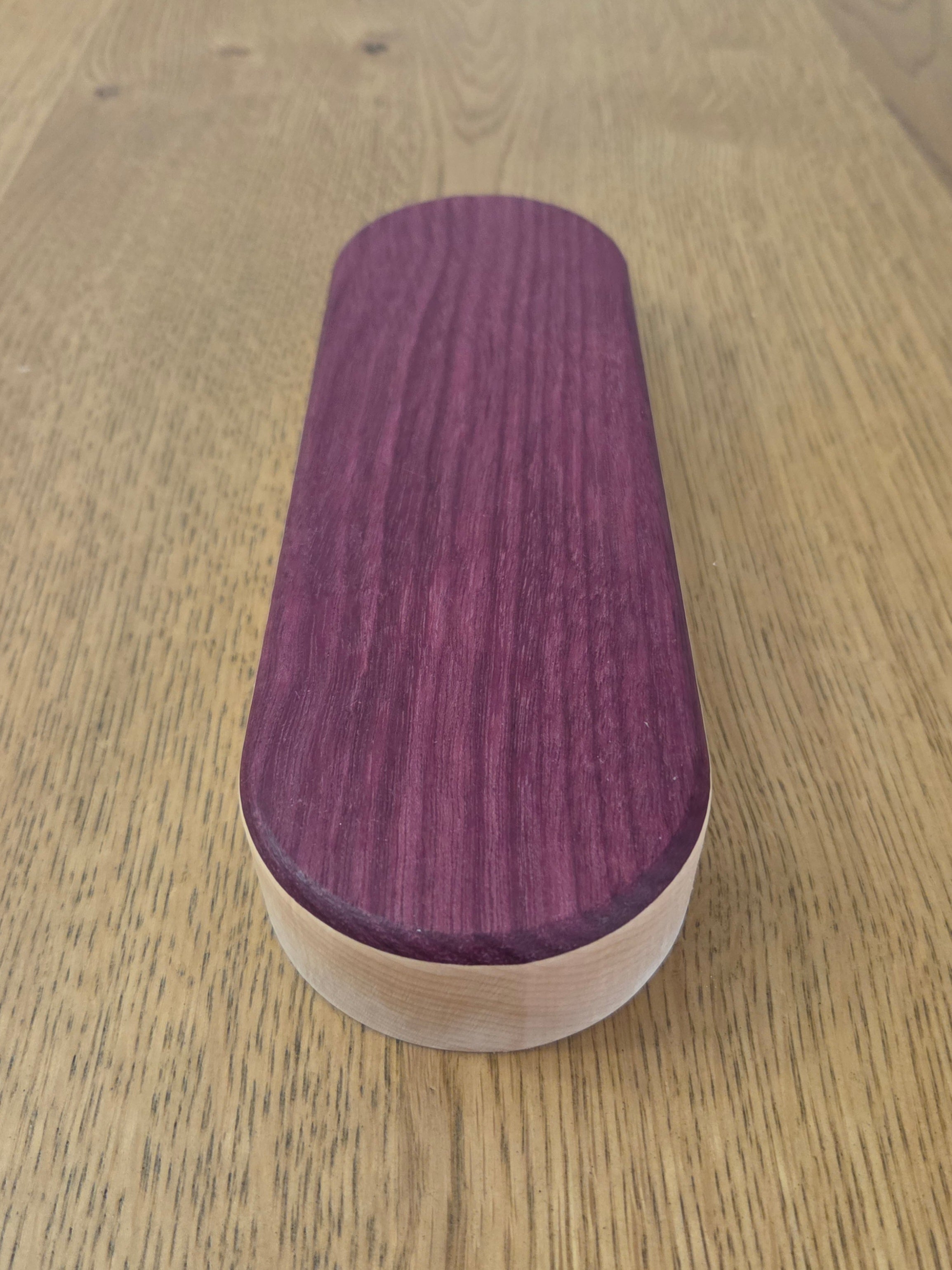 Oval-shaped wooden object with a purple top and white bottom on a light oak-colored surface