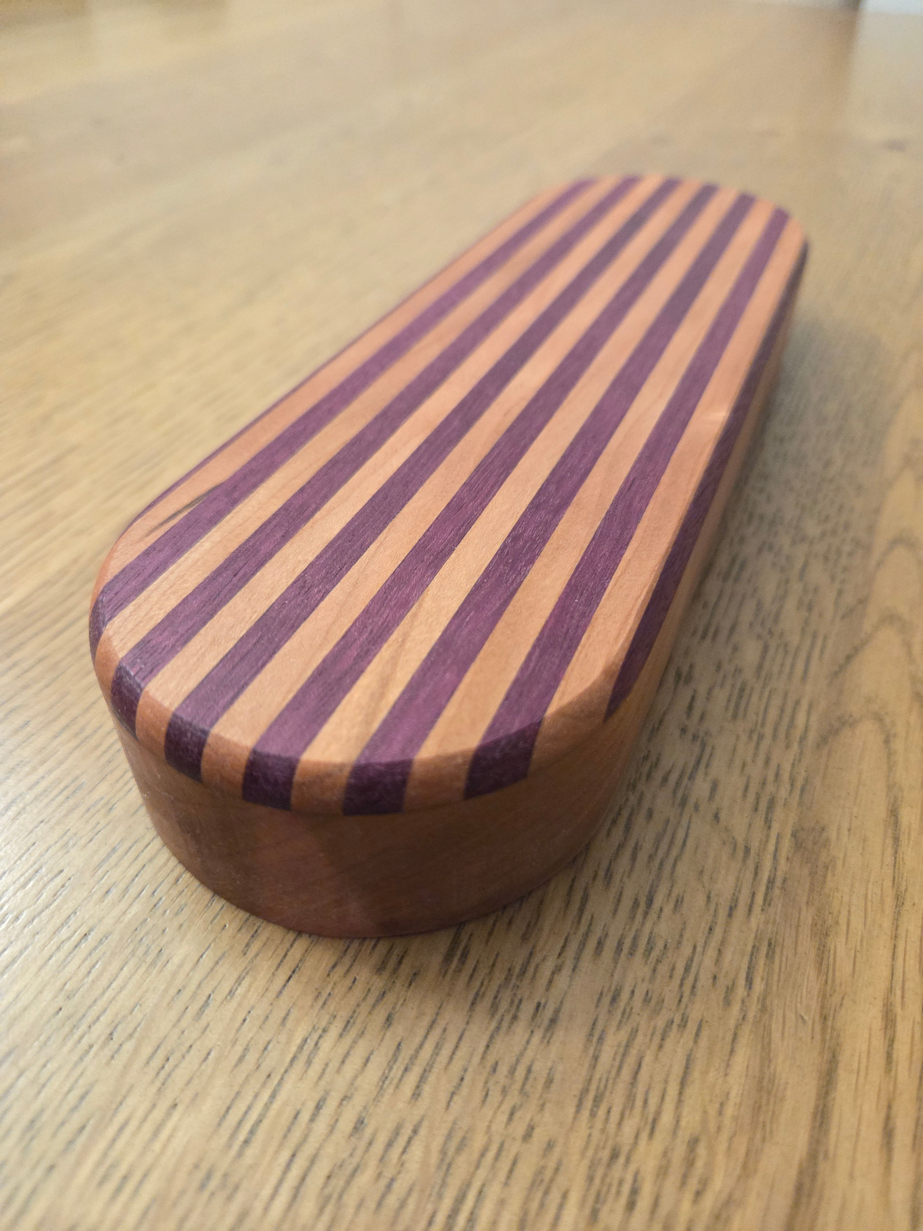 Oval-shaped wooden object with purple  heart and cherry wood stripes on top and a solid cherry wood bottom
